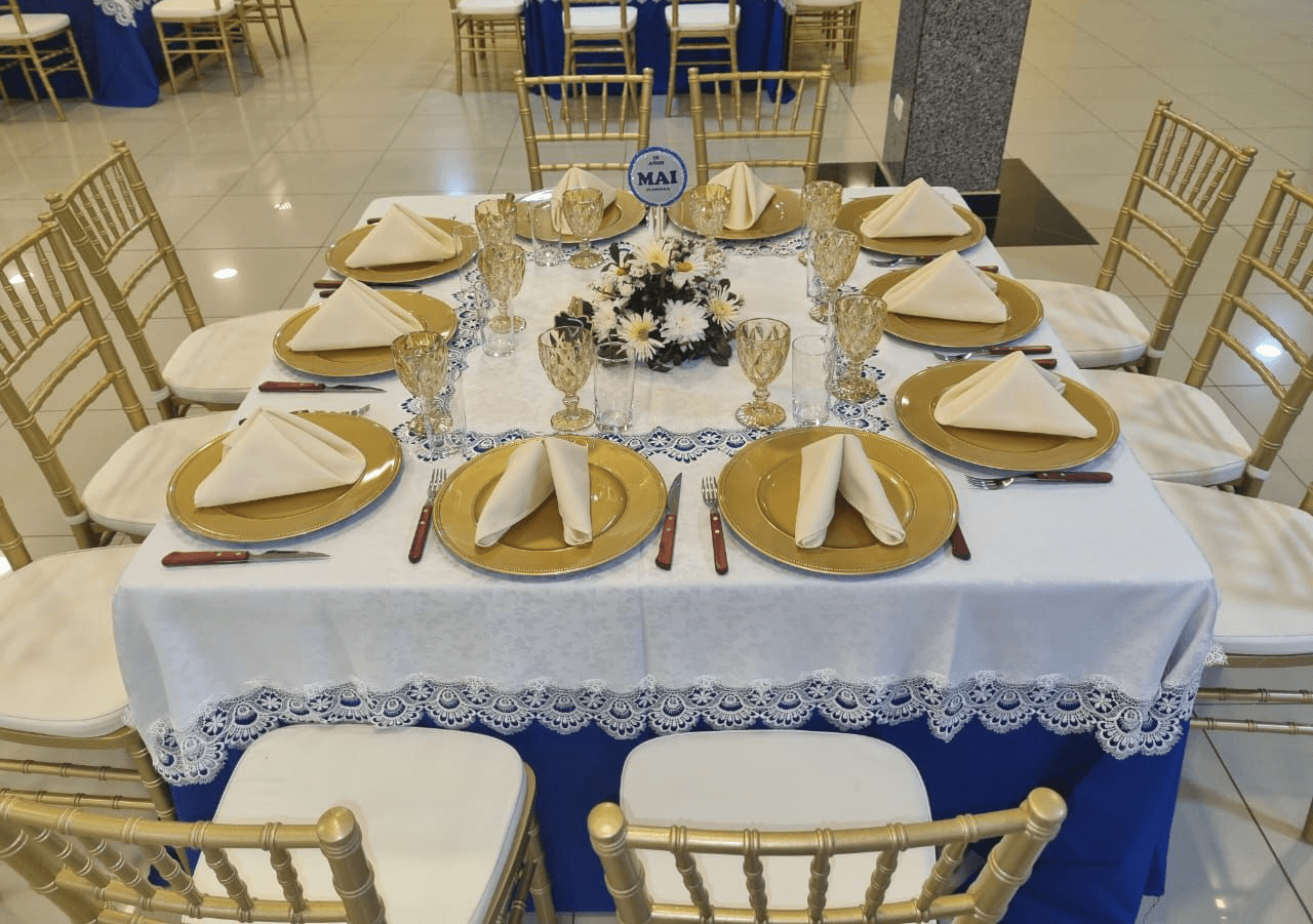 Mesa con mantel blanco y azul, platos dorados y sillas Tiffany